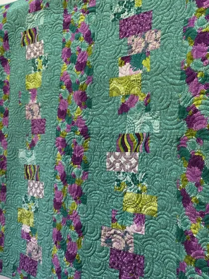 A beautiful quilt in shades of teal and purple, hanging on a wall.