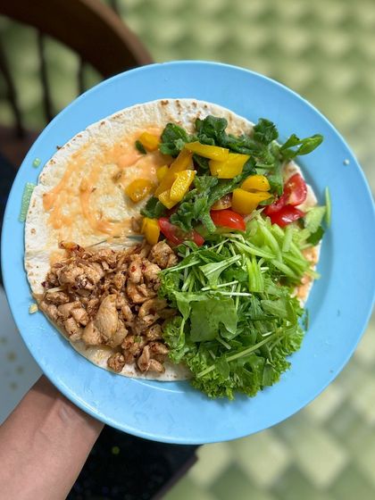 The making of a delicious chicken taco wrap, with seasoned chicken breast, fresh lettuce, arugula, and bell peppers on a whole grain tortilla.