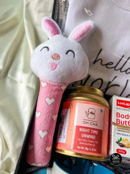 A close-up of the adorable pink bunny rattle and 'Night Time Unwind' tea from a mom-to-be hamper. I focus on including items for both relaxation and the baby.
