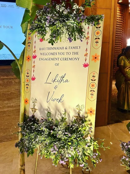 A beautiful welcome to an engagement ceremony, with a custom sign framed by lush purple flowers and traditional banana plants.
