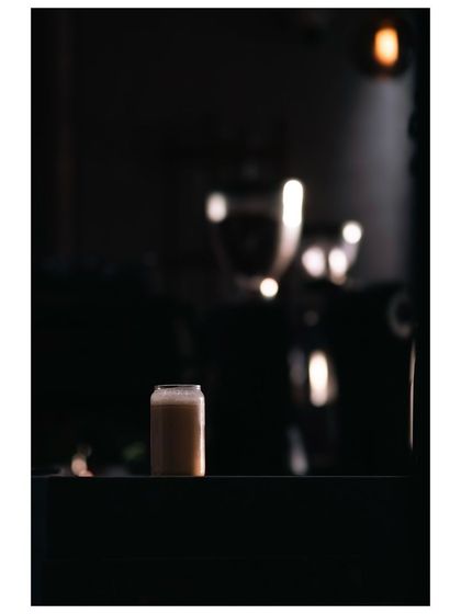 A minimalist photo of a single iced coffee, isolated by light in a dark cafe. The simple composition and dramatic lighting make the drink the hero of the shot.