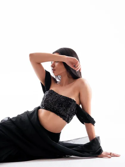 An artistic and slightly abstract pose. The composition, with the model's arm obscuring her face, creates a sense of mystery and focuses attention on the texture of the outfit.