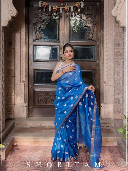 A beautiful blue linen saree with delicate white floral embroidery. This model shot shows how the saree drapes gracefully, making it perfect for any elegant occasion.