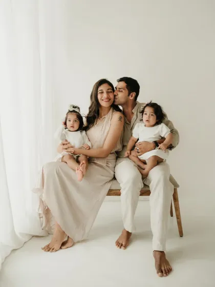 A sweet kiss for mom from dad while they hold their twin girls. This candid family photoshoot captures a moment of love and happiness.