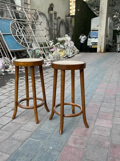 A pair of classic bar stools with turned legs and a caned seat, crafted from solid teak.