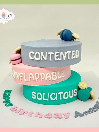 A modern and quirky three-tiered cake with words like "Contented," "Unflappable," and "Solicitous" for Ambrish's birthday.