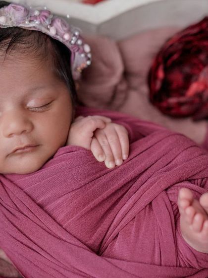 Dreaming of roses. This close-up shows the baby's tiny feet and hands, perfectly contained within a cozy magenta swaddle.