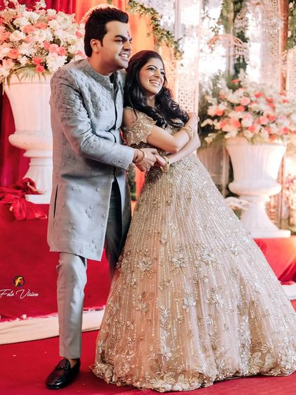 A full-length shot of the couple sharing a happy hug in front of a grand floral backdrop at their engagement.