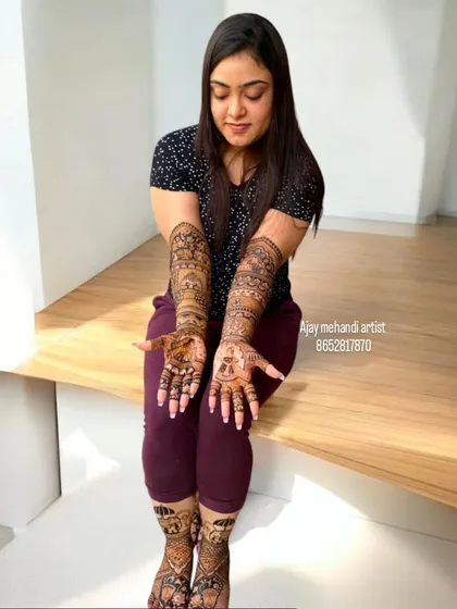 A relaxed pose showing the full extent of the bridal mehndi on both arms and legs. The designs are detailed and create a beautiful, complete look.