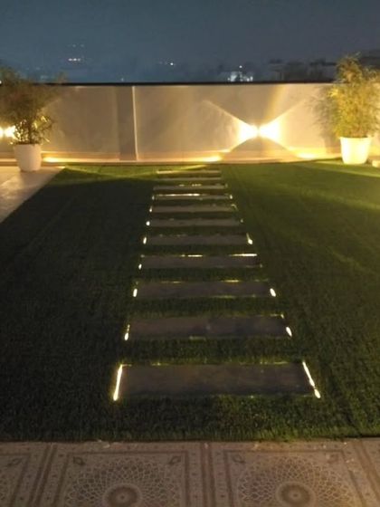 Lighting is a must. An illuminated pathway made of stepping stones on artificial grass, with wall-mounted up-and-down lights creating a beautiful effect on the boundary wall.