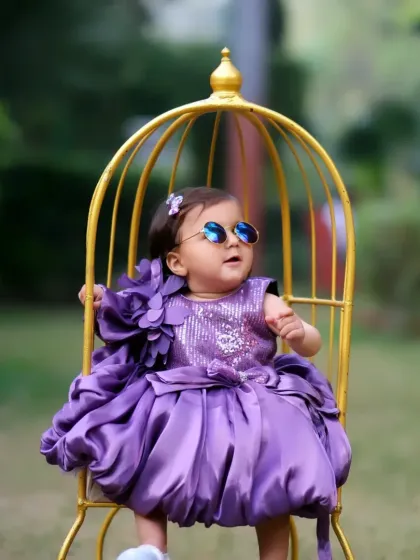 A stylish little girl in a purple dress, posing in our golden birdcage prop. The outdoor garden setting adds a touch of magic to the scene.