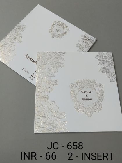 A simple white invitation with a silver foil floral wreath for the monogram. The design is clean, fresh, and perfect for a minimalist wedding aesthetic.