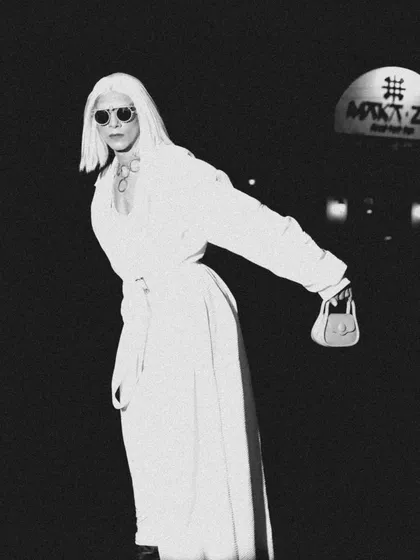 A grainy, black and white shot that gives a vintage, paparazzi-style feel. The model's confident pose and all-white outfit create a striking image against the night's darkness.