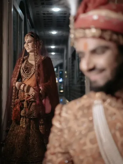 A creative shot with the bride in focus in the background and the groom's smiling face blurred in the foreground, telling a story of anticipation.