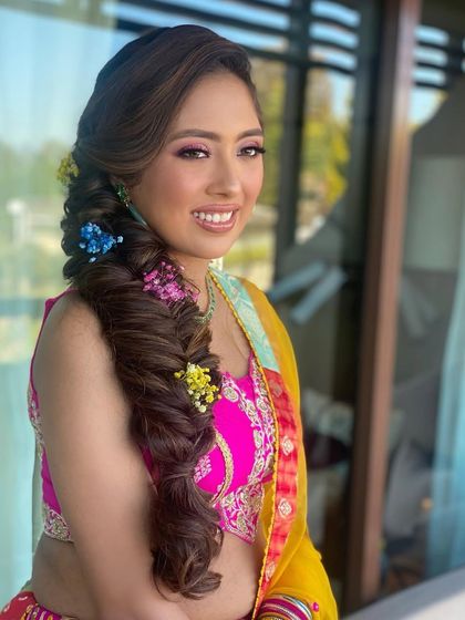Popping colors for a Mehendi look! This side-swept fishtail braid is adorned with vibrant flowers, adding a playful and colorful touch that’s perfect for the celebration.