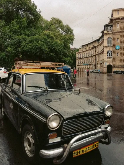 A Kaali-Peeli taxi parked in the rain in front of the historic Horniman Circle. The wet, reflective ground and grand architecture create a beautifully atmospheric and classic Bombay photograph.