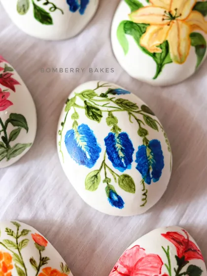 A close-up of a marzipan egg featuring a delicate blue pea flower vine.