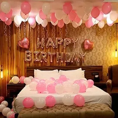 This birthday room decoration shows a softer, elegant color scheme using pink and white balloons. The foil "Happy Birthday" sign is complemented by heart-shaped balloons and warm lighting, creating a chic and celebratory feel.