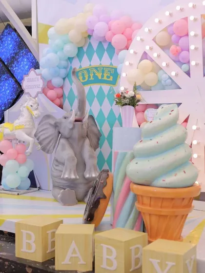 A close-up of the pastel carnival stage, showing the giant ice cream prop, a playful elephant, and "BABY" blocks. The soft colors and whimsical elements are perfect for a first birthday.