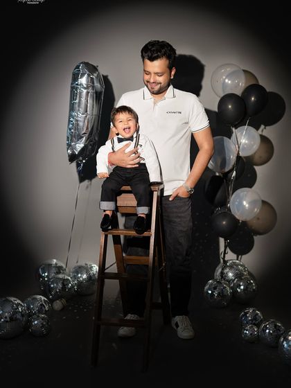 A fun father and son portrait for a first birthday celebration. The disco balls and number '1' balloon add a festive, party atmosphere.