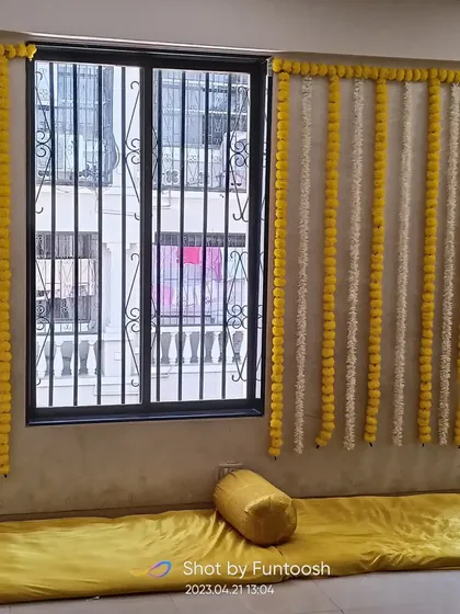 For simple home Haldi functions, we create clean and elegant decor like these alternating yellow and white flower strings against a wall.