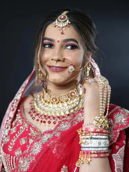 A classic bridal portrait. This look features a traditional red lehenga, complete with a nose ring, maang tikka, and bold red lip. The makeup is glamorous and designed to be picture-perfect.