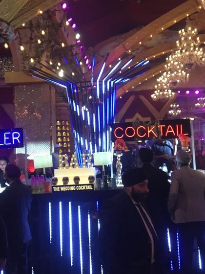 A massive, multi-station bar setup for a large wedding, featuring dedicated areas for molecular cocktails and general drinks, all under dramatic neon and structural lighting.