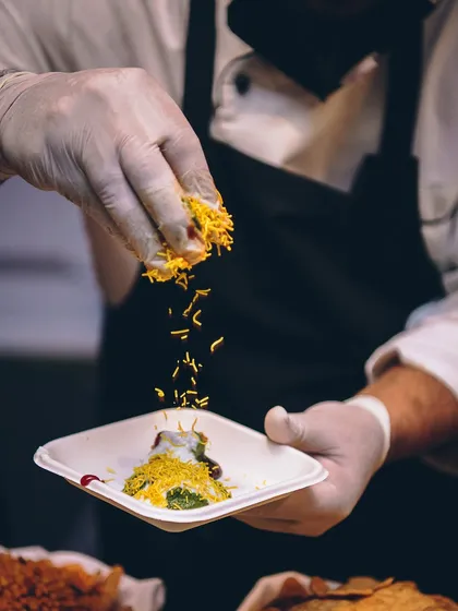 A chef sprinkles a final garnish on a plate of Indian chaat, adding texture and flavour.