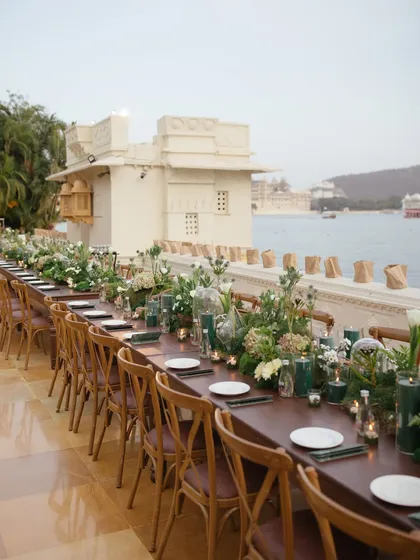 An elegant, long-table setup for a welcome dinner by the waters of Lake Pichola in Udaipur. We create relaxed yet sophisticated atmospheres for guests to mingle, with details like custom menus and ambient lighting.