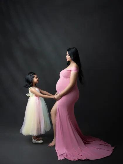 A touching moment between a mother and her daughter as they wait for the new baby. This portrait highlights the special bond they share, with the daughter gently holding her mother's hand on the baby bump.
