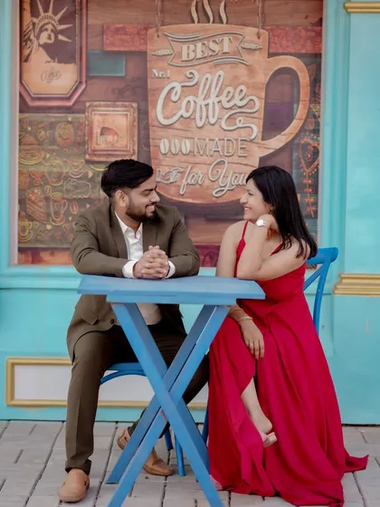 A playful moment sharing a drink against a vibrant blue door, reminiscent of a European street. The woman's bright red dress pops against the cool tones, creating a lively and stylish pre-wedding photo.