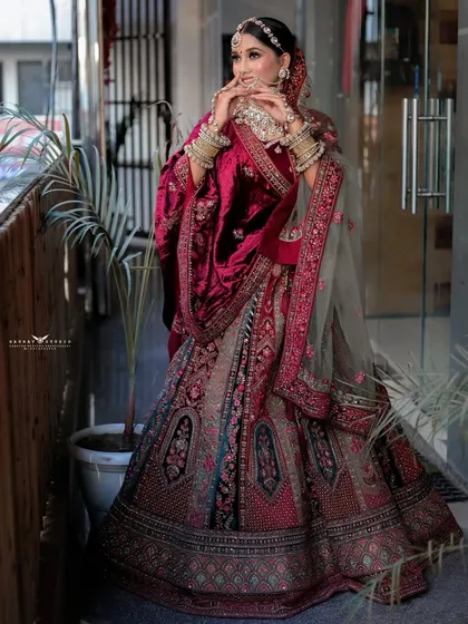 A dynamic pose showing the bride interacting with her lehenga, highlighting the rich fabric and intricate work.