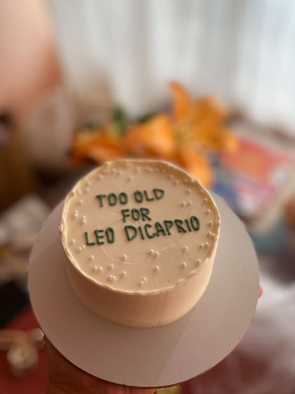 A funny and topical bento cake that reads "Too old for Leo DiCaprio." It's a great example of the custom, humorous designs I can create.