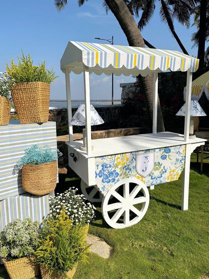 A charming cart with a striped awning and floral print, used as a serving station for the outdoor event.