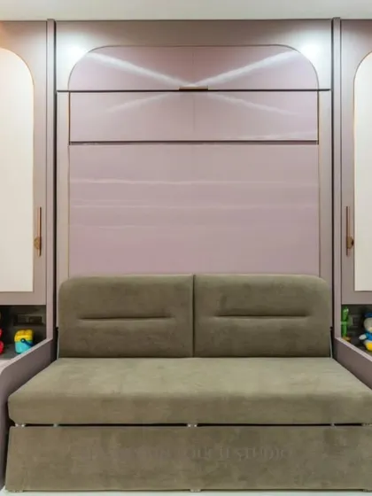 This room features a comfortable sofa that is part of a larger Murphy bed unit. The surrounding cabinetry, with its arched motifs and soft colors, provides ample storage for toys and books, making it a perfect kids' room or guest room.