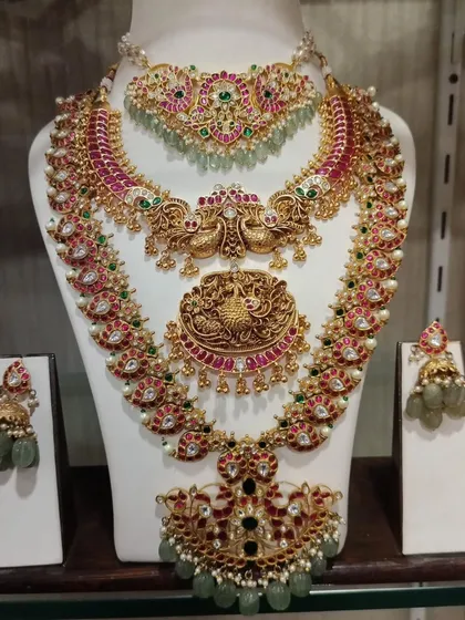 This is a complete South Indian bridal set, featuring traditional temple jewellery designs with intricate peacock motifs. The set includes a choker, a long haram, a stunning pendant, matching jhumkas, and a maang tikka, all crafted to look like authentic gold.