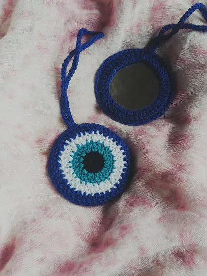 This crochet evil eye bag charm does more than just look good, it also has a small mirror tucked inside for quick touch-ups. It's a unique and practical accessory to hang on your favorite bag.