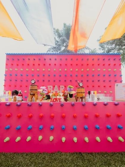 A fun and colorful bar setup for a pre-wedding event. The bright pink bar is decorated with a pegboard-style wall, adding a playful and interactive element.