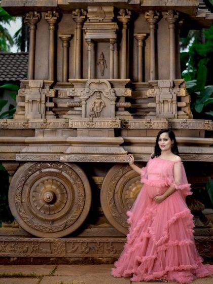 This pink ruffled maternity gown looks stunning against the traditional architecture of a stone chariot, blending modern fairytale style with timeless heritage.