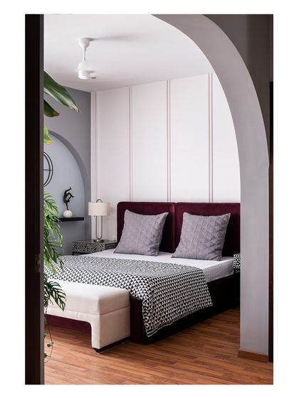 An arched entryway leads into the master bedroom, revealing a deep mauve velvet bed set against a minimally designed wall. This architectural feature creates a sense of arrival and frames the serene space within.