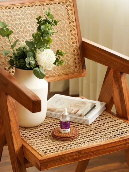 A lifestyle shot of a face serum placed on a stylish rattan chair next to a vase of flowers. This composition integrates the skincare product into a chic, modern home environment, highlighting its aesthetic appeal.