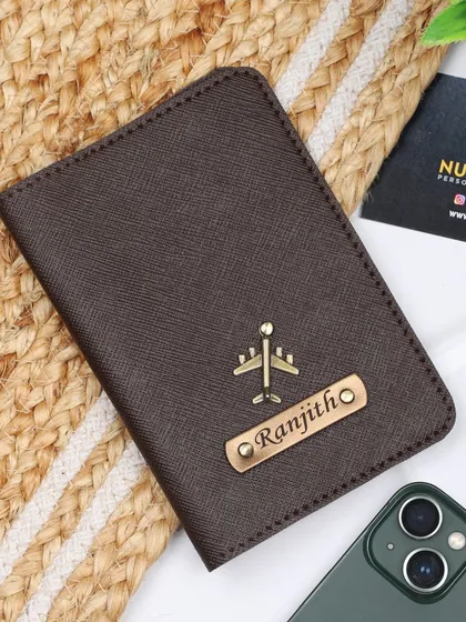 This personalized passport cover in a classic brown color features an airplane charm and a custom engraved name.