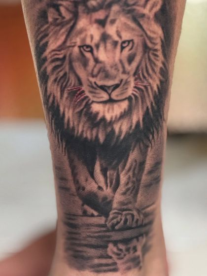 A close-up of the lion's face in the leg tattoo, focusing on the detailed shading in the fur and eyes.