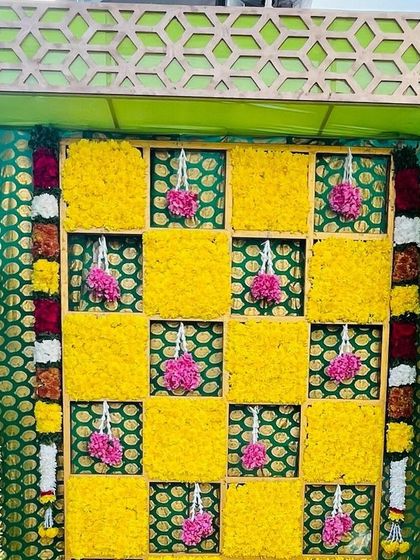 A close-up of a Haldi backdrop, showing the checkerboard pattern of yellow marigolds and hanging pink floral tassels. The intricate design adds a beautiful texture to the decor.