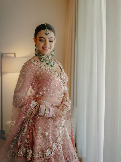 A beautiful portrait by the window. The natural light catches the soft shimmer in her makeup, highlighting her flawless skin and the intricate details of her pastel bridal look.