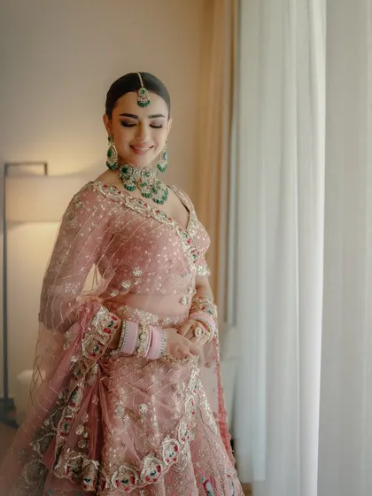 A beautiful portrait by the window. The natural light catches the soft shimmer in her makeup, highlighting her flawless skin and the intricate details of her pastel bridal look.