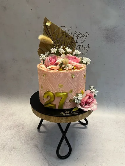 This peach-colored beauty has a subtle textured pattern on the buttercream. It's decorated with fresh pink roses, dried botanicals, and a gold '27', making it a chic cake for a birthday celebration.
