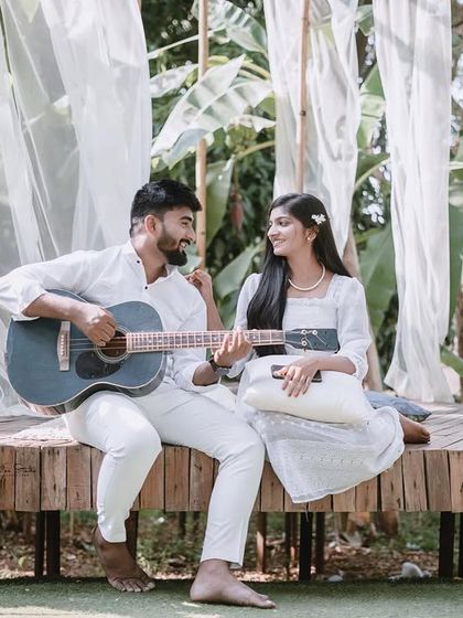 A beautiful, wide shot of a picnic-style setup on a wooden deck. The white drapes and natural greenery create a bohemian and romantic atmosphere.
