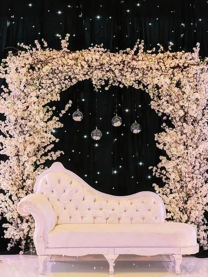 A romantic and dreamy engagement photo booth. We created a large arch of white cherry blossoms against a starry black cloth, with a classic white chaise lounge for couple portraits.