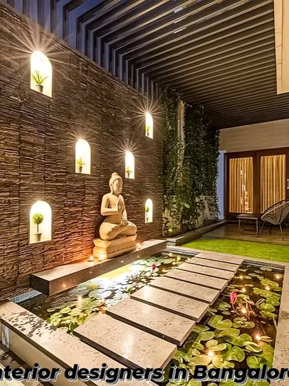 A serene and tranquil patio design featuring a stone accent wall with illuminated niches. The central water feature with a Buddha statue and lily pads creates a peaceful, meditative atmosphere.